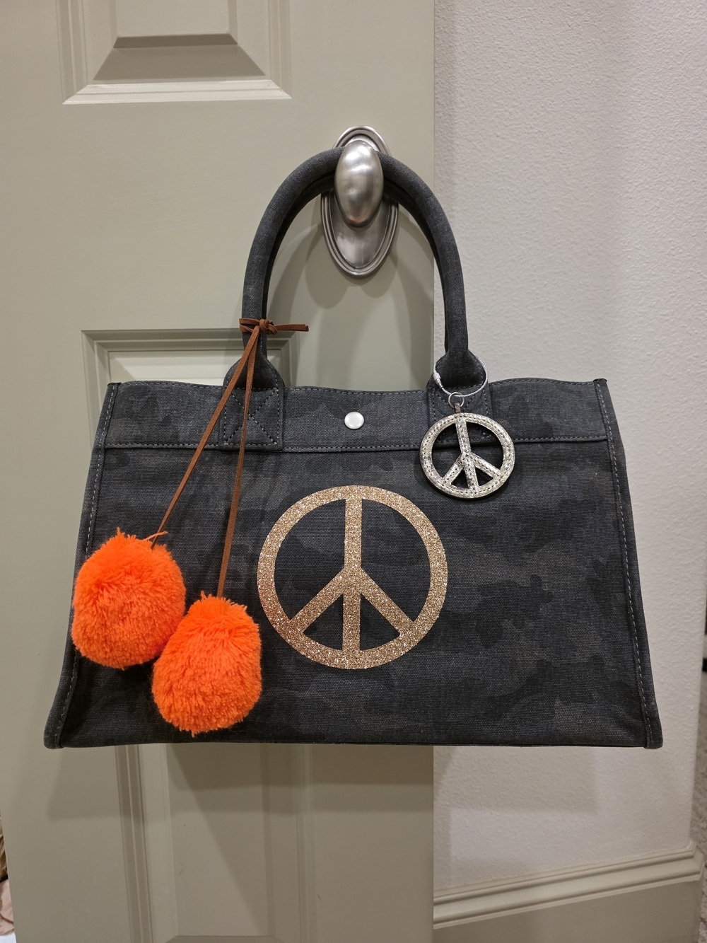 Camo Canvas Tote with Gold Peace Emblem and Orange Pom-Pom Accents